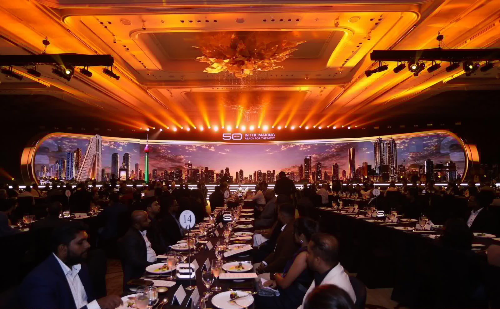 A ballroom gala with a curved LED wall and golden stage lighting