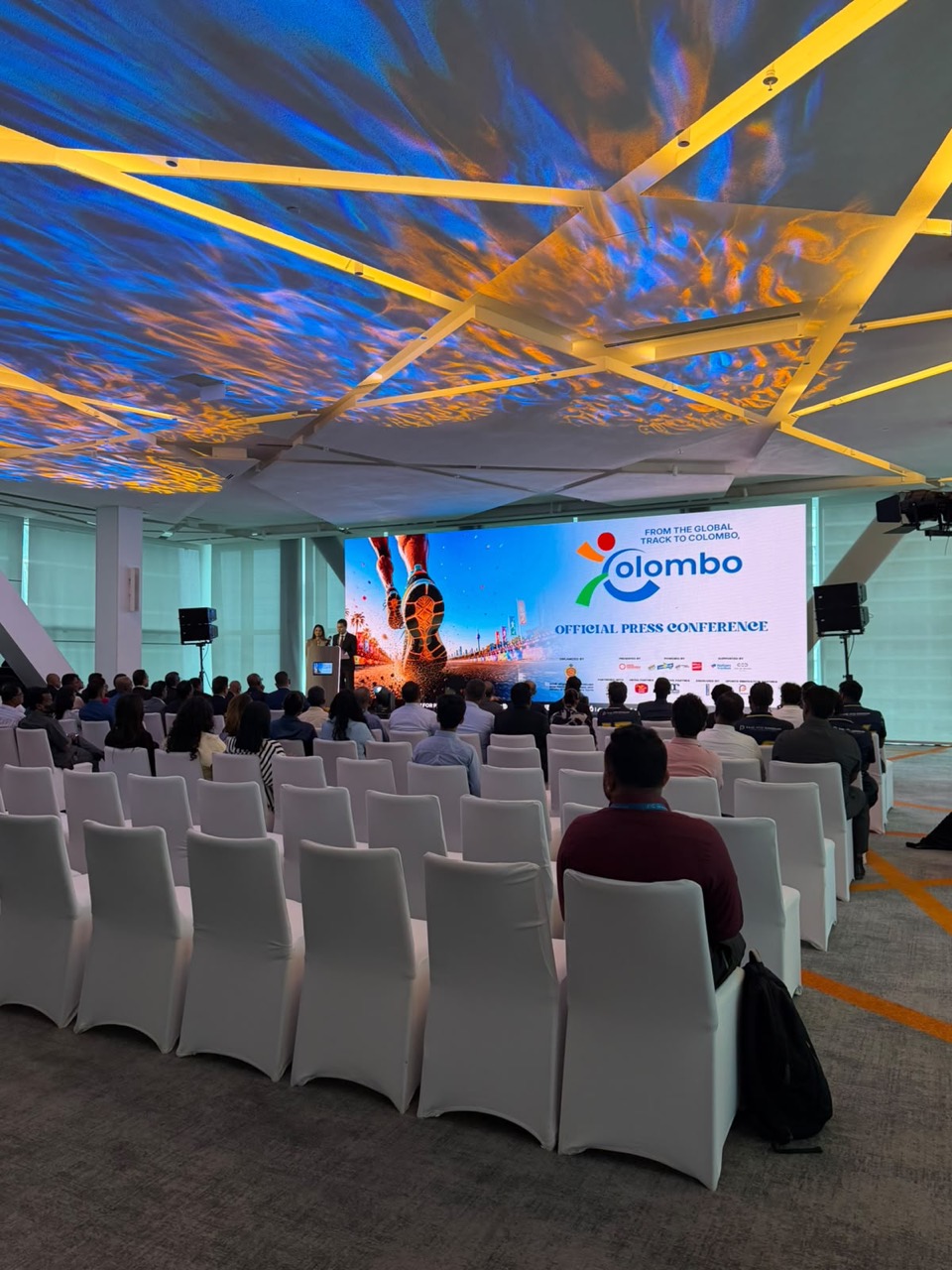 Press conference with an LED screen, speakers and white chair covers