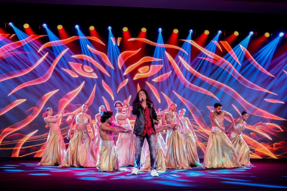 A singer and dancers in front of a vivid LED backdrop with blue and red beams